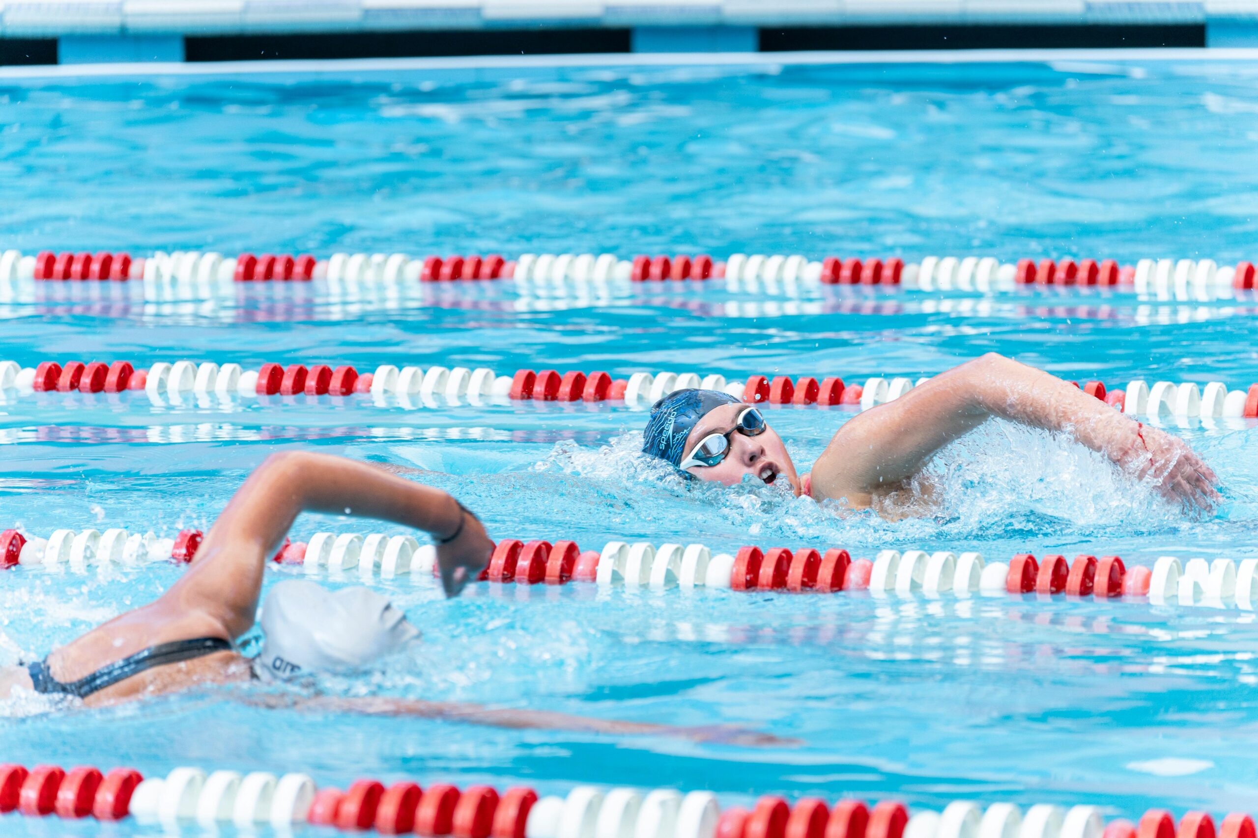 Two athletes swimming competitively in a clear outdoor pool, showcasing speed and technique.